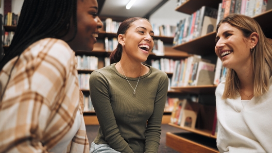 Three students talking and laughing in a library.